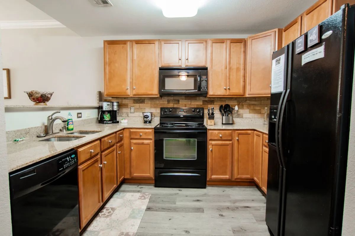 A modern, fully equipped kitchen with sleek black appliances, granite countertops, wood cabinetry, and a central kitchen island. The setting is bright and practical, ideal for meal preparation and social interaction.