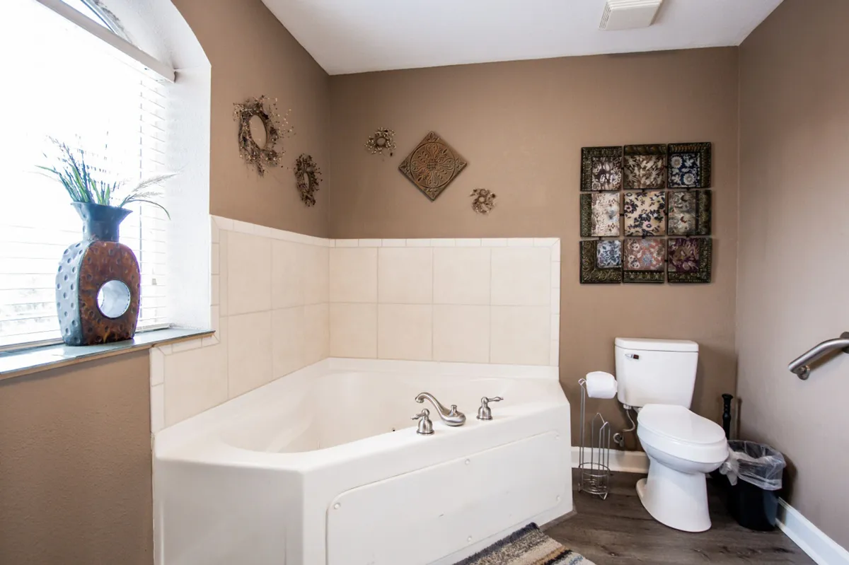A tranquil bathroom scene with a luxurious jacuzzi tub, decorative wall art, and a window allowing natural light to fill the space. The setting exudes relaxation and comfort.