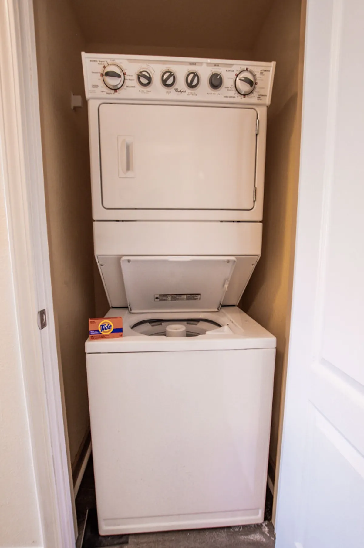 A stacked washer and dryer set with detergent ready for use, situated in a tidy laundry nook. The setup underscores convenience and modern comfort for guests.